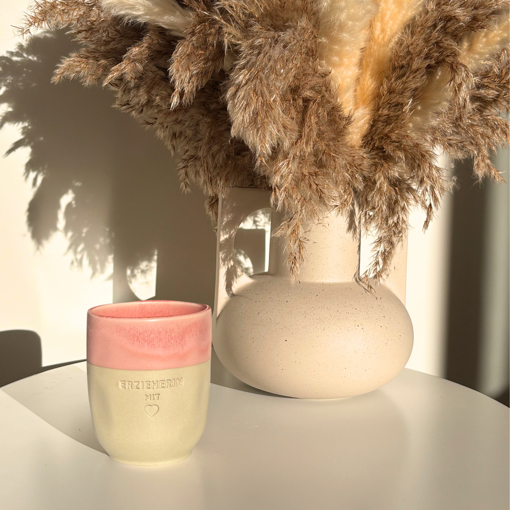 Steingut-Becher in Dawn Pink mit rosa reaktiver Glasur, neben Trockengräsern – Gravur „Erzieherin mit Herz", Erzieherin Geschenk zum Abschied